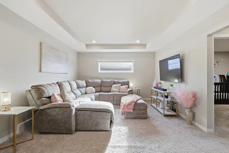 Bright basement living room with sectional sofa, tray ceiling, and soft natural light