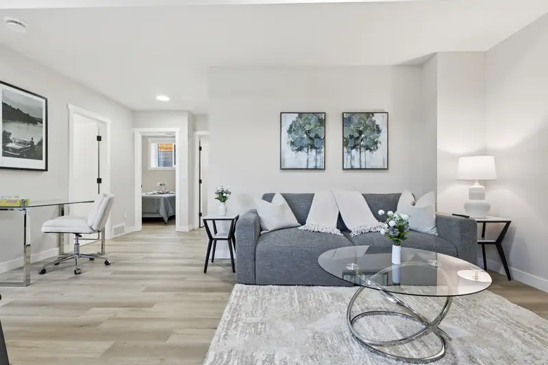 Bright open living area with grey sofa, framed art, and view into bedroom
